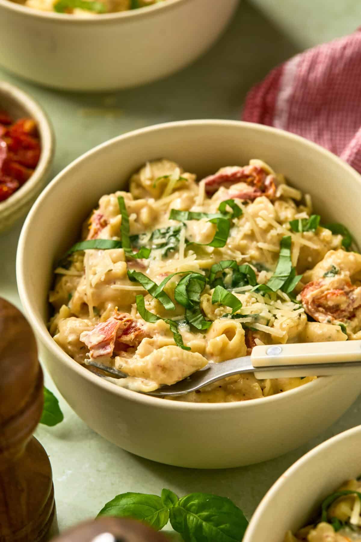 Pasta in a bowl with a utensil for serving with basil strips on top and other bowls around. 