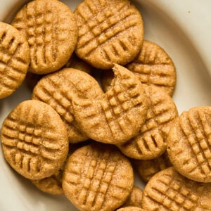 Peanut butter cookies on a plate and the top one has a bite taken out of it.