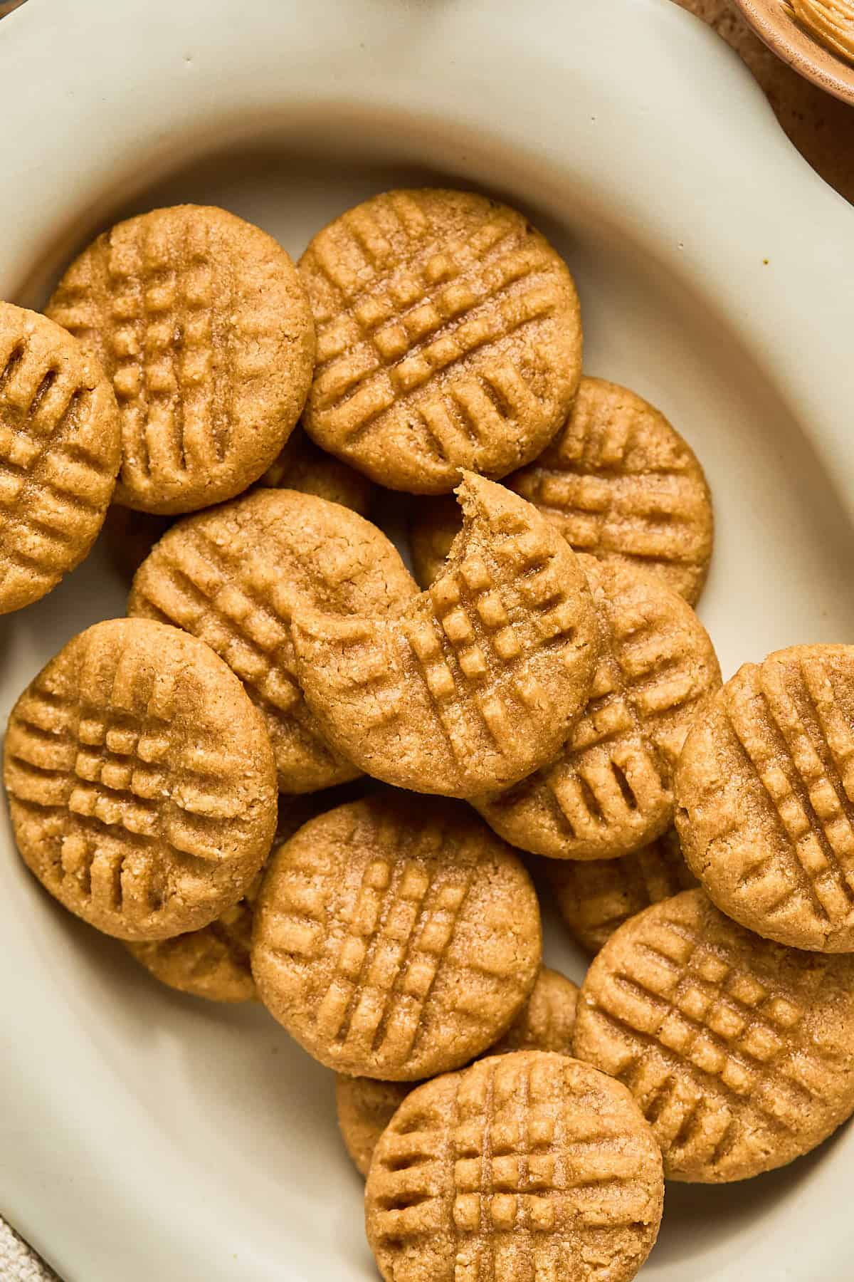 Peanut butter cookies on a plate and the top one has a bite taken out of it.