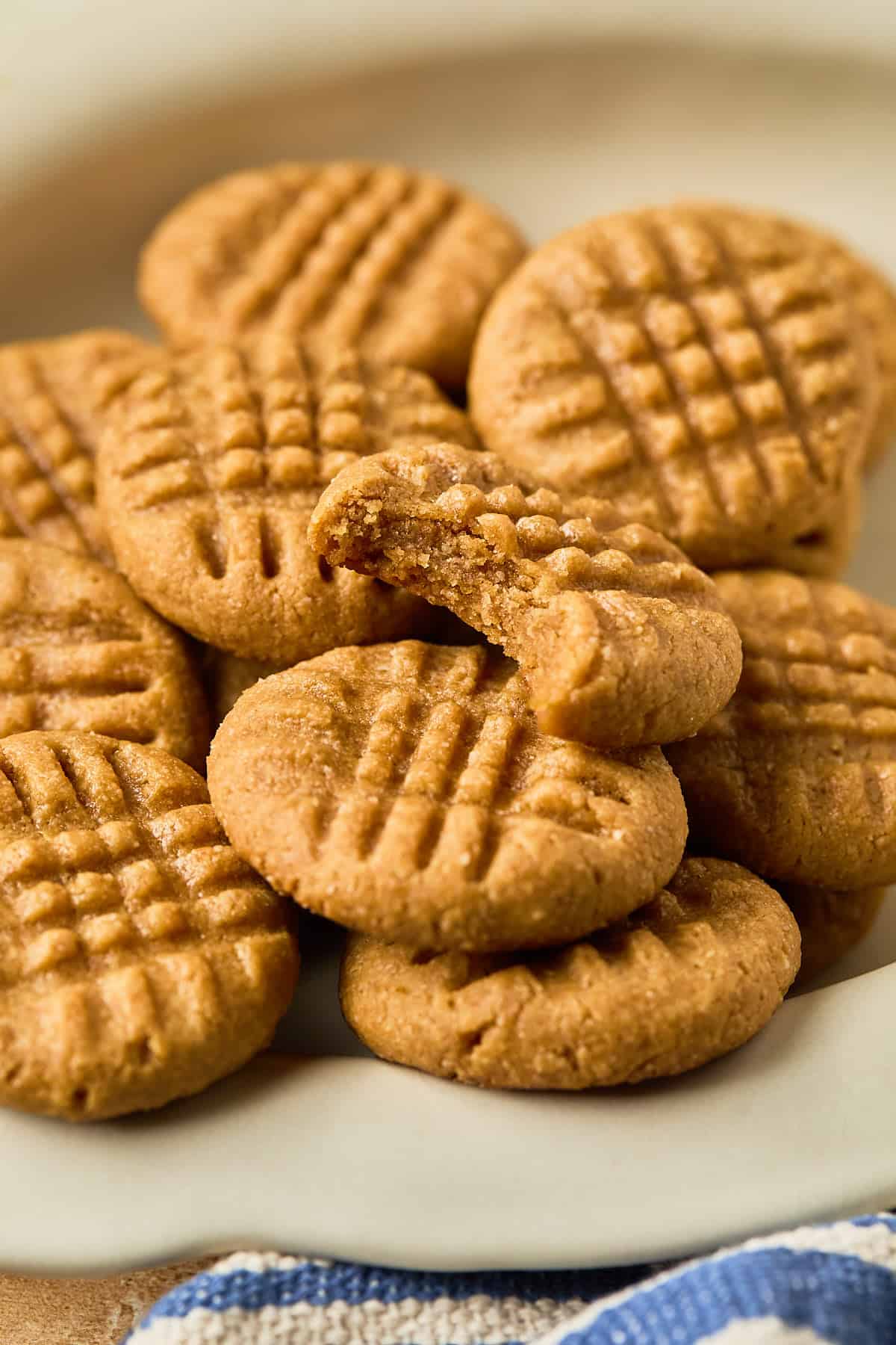 Peanut butter cookies stacked on a plate and the top one has a bite taken out of it.