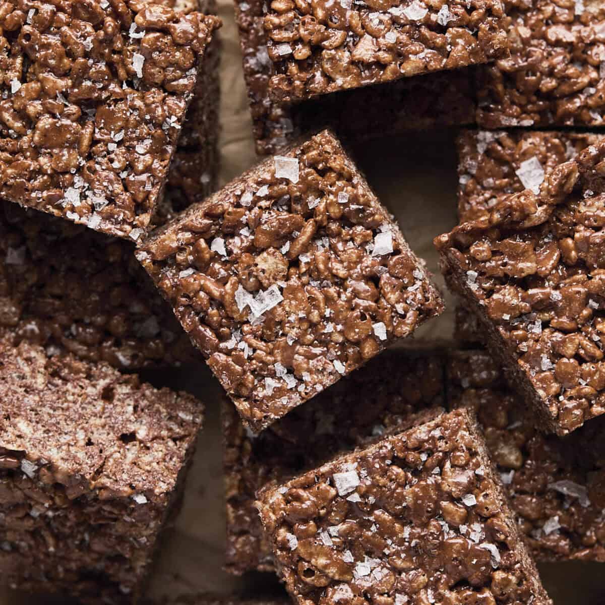 Chocolate rice krispie treat squares laid out with some overlapping and flakey sea salt on top.