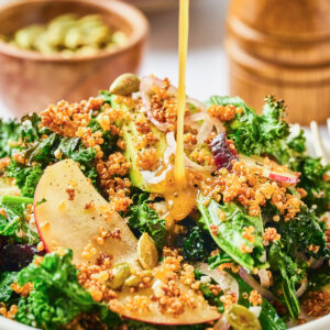 Crispy quinoa salad with apples and dressing being poured on top.