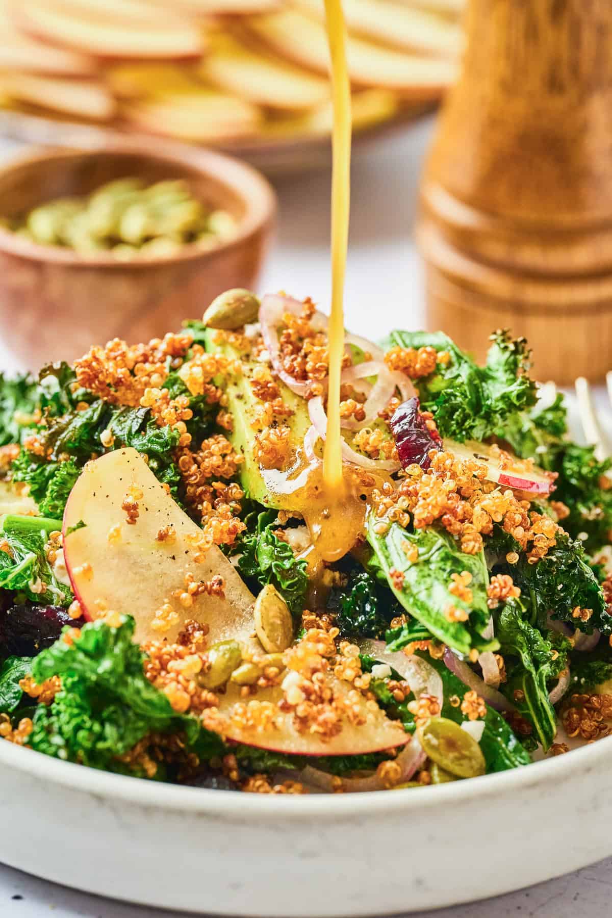 Crispy quinoa salad with apples and dressing being poured on top.