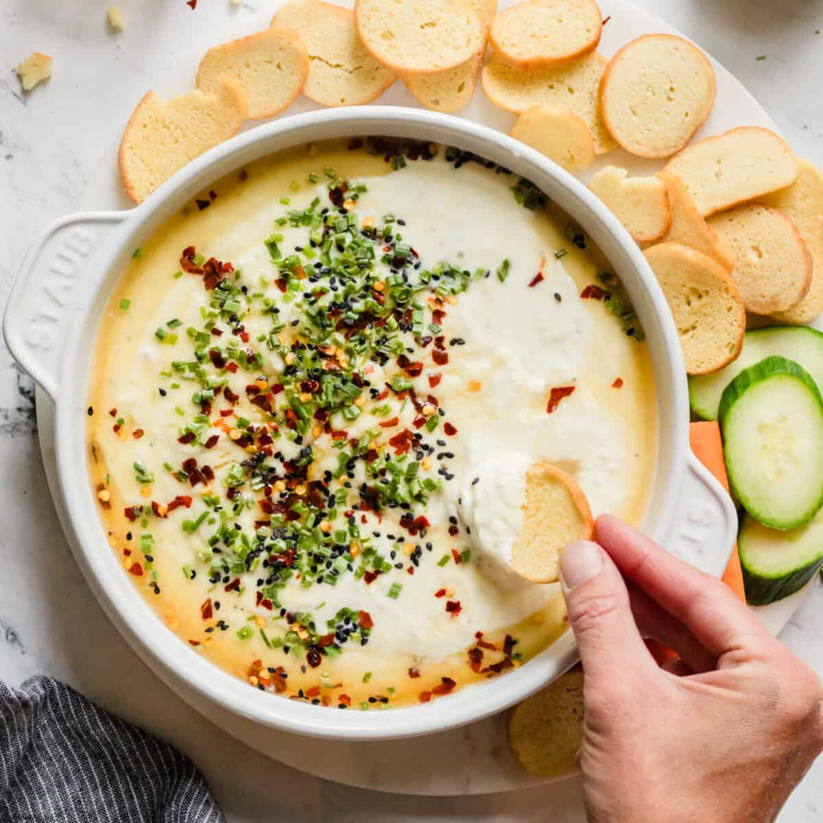 Bowl of creamy dip with chives and honey on top and a hand scooping some out with a cracker.