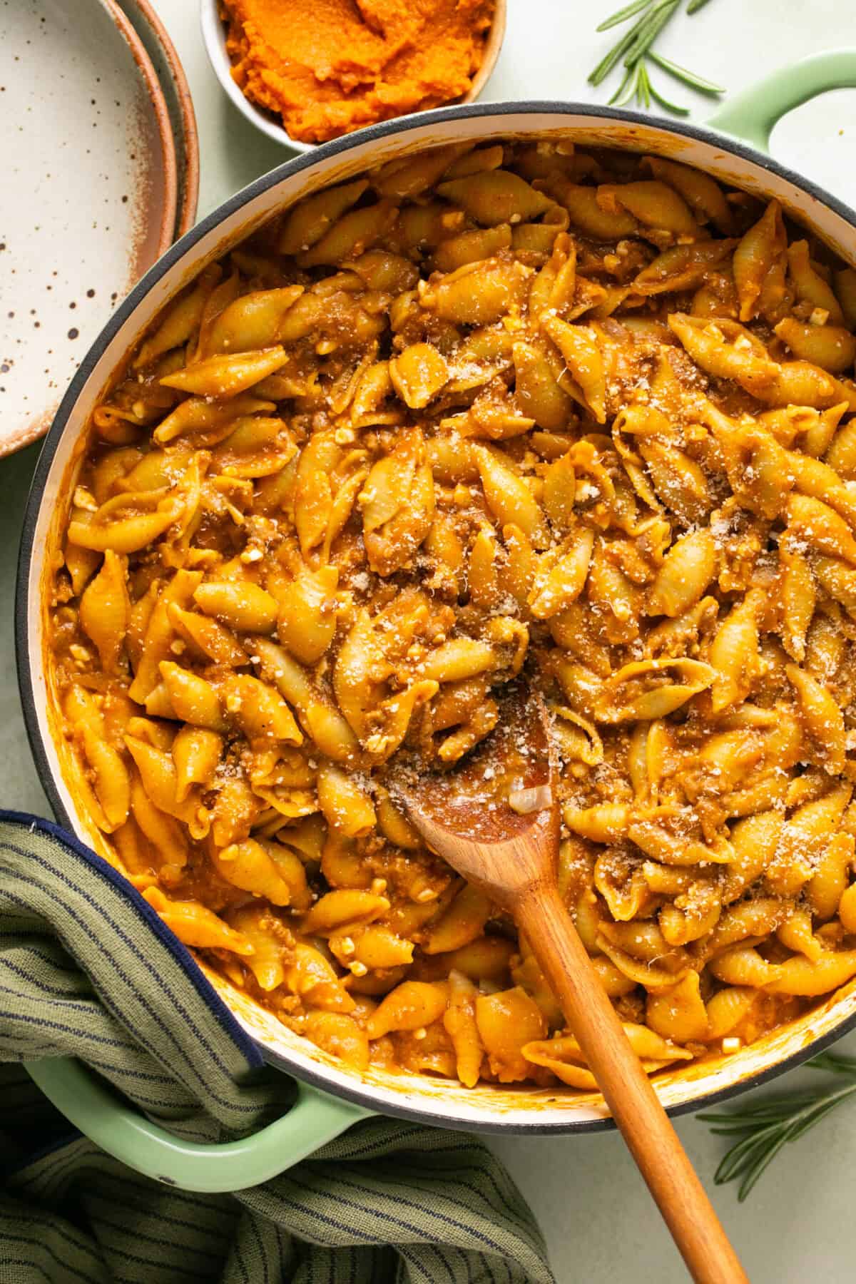 Creamy pumpkin beef pasta in a large skillet with parmesan cheese and a spoon for serving.  