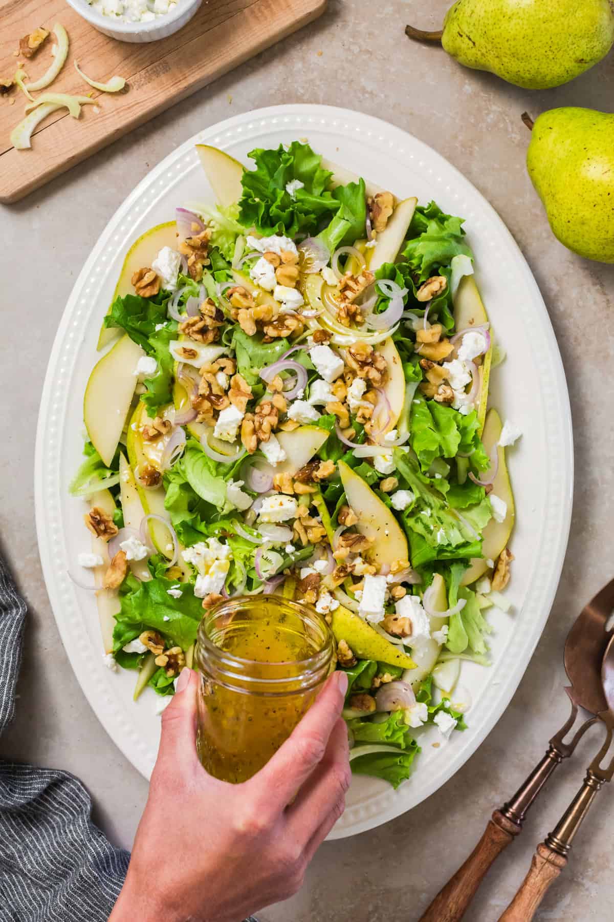 Salad with walnuts, feta and sliced pears on a serving dish with dressing being poured on top.