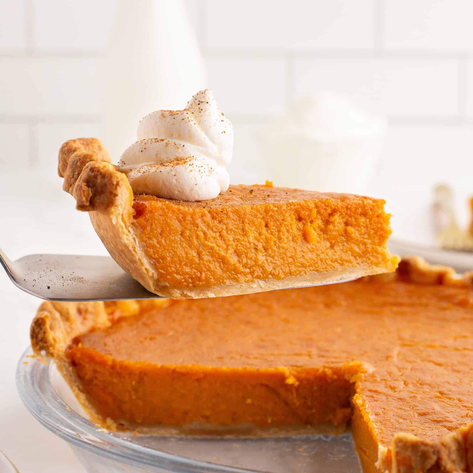 A slice of pie being served from the dish with whipped cream on top.