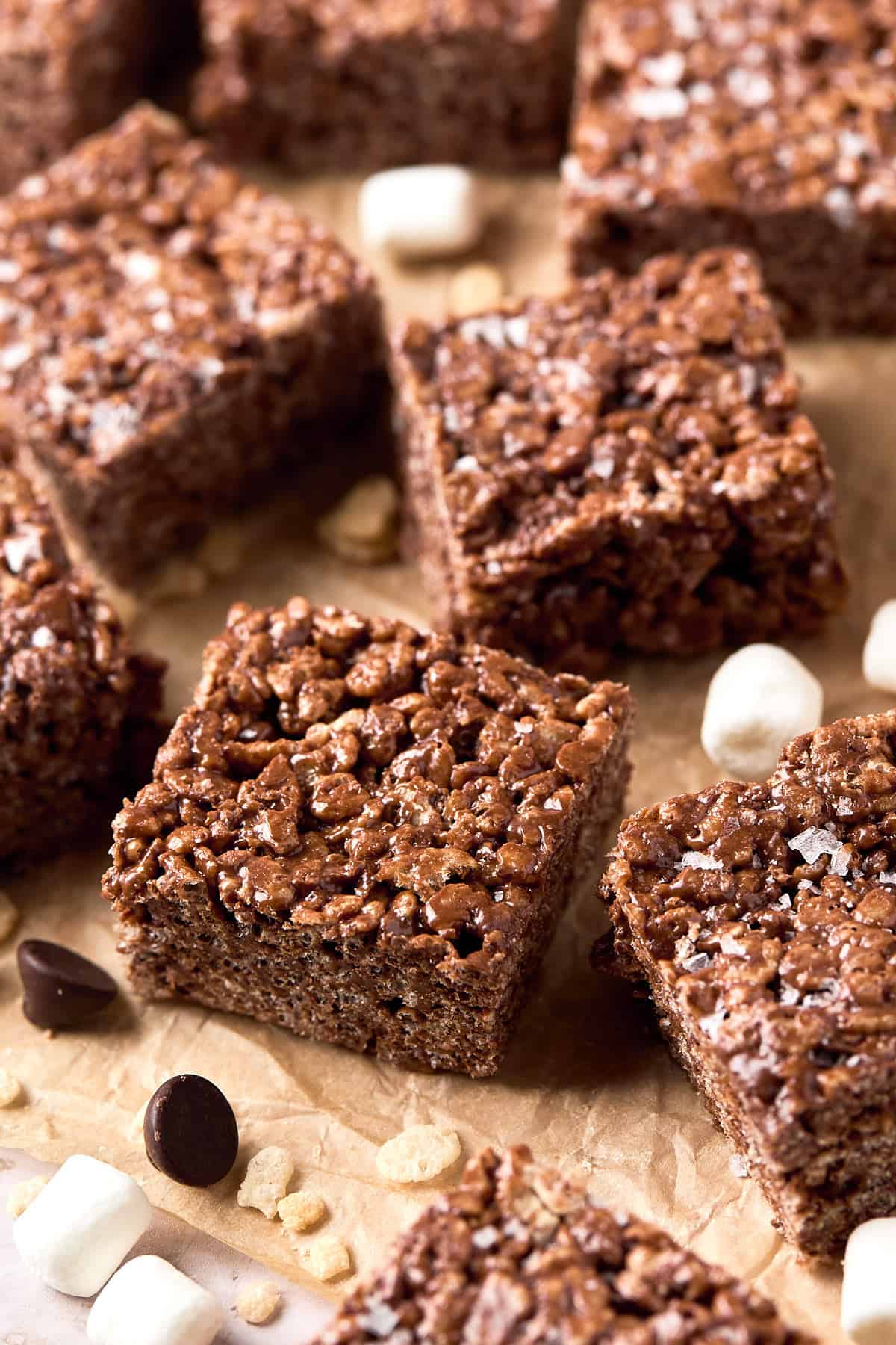 10 chocolate rice krispie treats on parchment paper with marshmallows and chocolate chips sprinkled around.