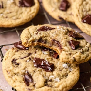 Close-up of chocolate chip coffee cookies on a wire rack. One cookie is stacked on another with a bite taken out, revealing a soft interior with chunks of chocolate. Sprinkles of sea salt are visible on top, adding texture and flavor.