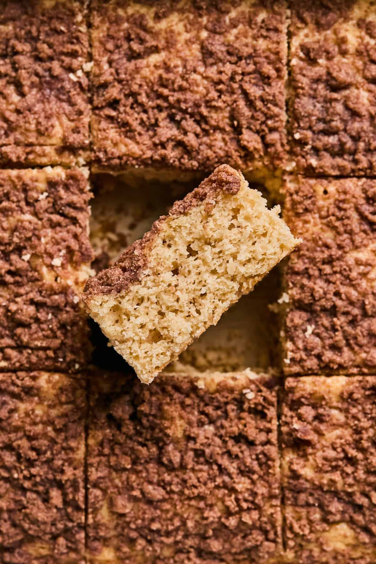 A close-up of a sliced applesauce coffee cake with crumb topping arranged in a grid pattern. One slice is slightly elevated, showcasing the moist texture and rich crumb layer.