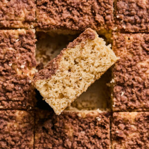 A close-up of a sliced applesauce coffee cake with crumb topping arranged in a grid pattern. One slice is slightly elevated, showcasing the moist texture and rich crumb layer.