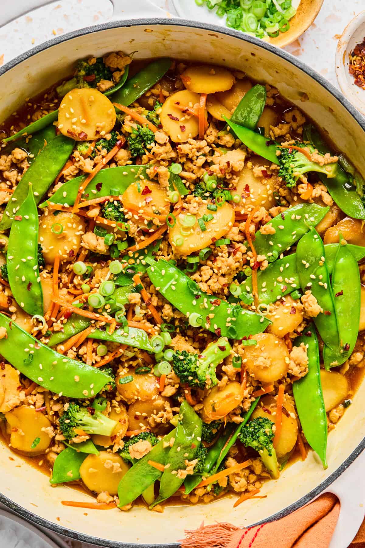 Colorful Ground Chicken Stir Fry with snap peas, broccoli, carrots, water chestnuts, and green onions, topped with sesame seeds in a large pan.