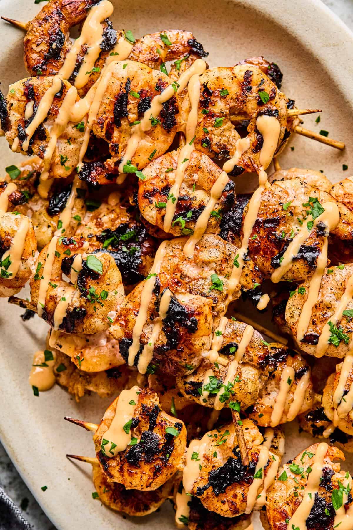 BBQ Prawn Skewers grilled to perfection, topped with a creamy, orange-colored sauce and garnished with chopped herbs, served on a light-colored oval plate.