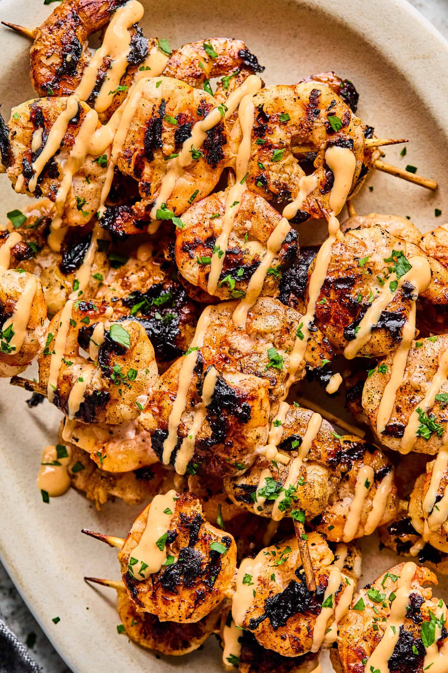 BBQ Prawn Skewers grilled to perfection, topped with a creamy, orange-colored sauce and garnished with chopped herbs, served on a light-colored oval plate.