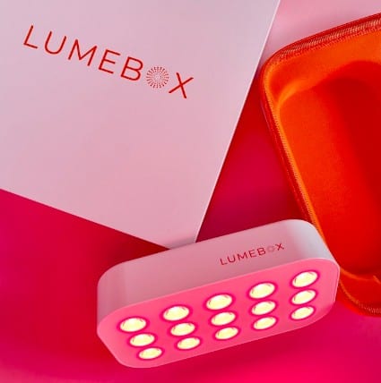 A small rectangular device labeled LUMEBOX emits pink light from multiple circular bulbs, next to an orange case and a white box featuring the brand name in orange text—check for discount codes to save on your purchase.