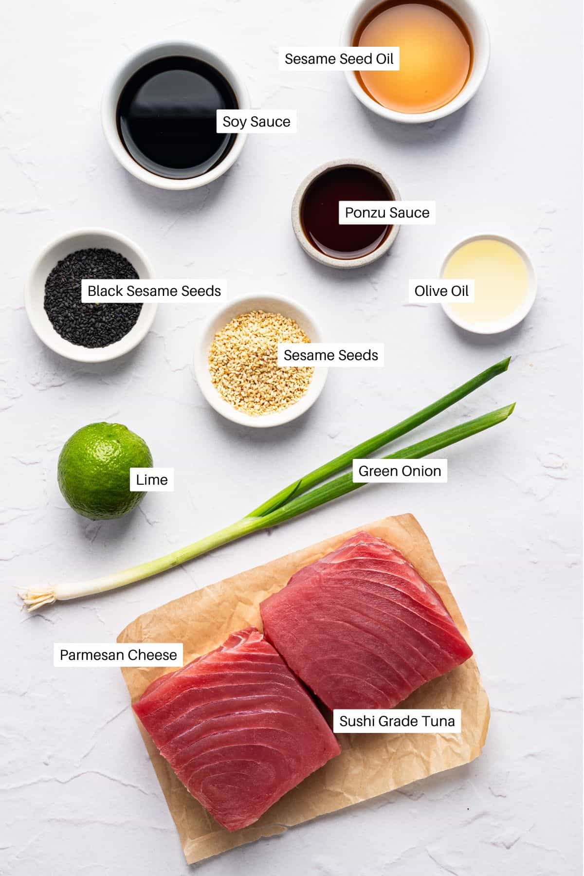 Overhead view of sushi-grade tuna on parchment, surrounded by ingredients like parmesan cheese, green onion, lime, baked chicken cutlets, black and white sesame seeds, soy sauce, sesame seed oil, ponzu sauce, and olive oilโeach labeled.