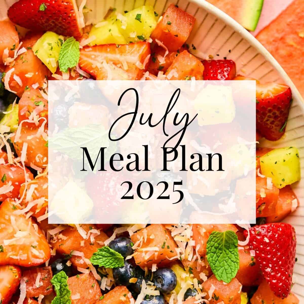 A colorful fruit salad with strawberries, blueberries, watermelon, pineapple, mint leaves, and shredded coconut. Over the image, text reads: July Meal Plan 2025 in elegant script and bold fonts.