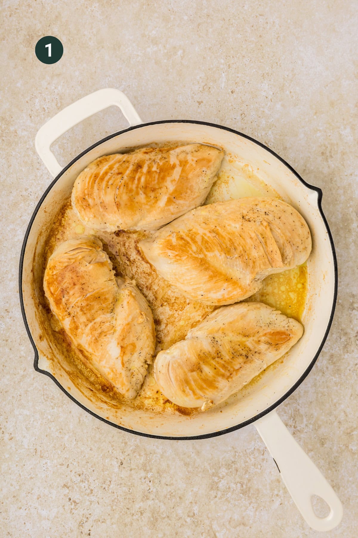 Four cooked chicken breasts are searing in a white skillet on a light countertop. The chicken is lightly browned with a hint of sauce, making it perfect for any balsamic chicken recipe. A small amount of liquid is visible in the pan.