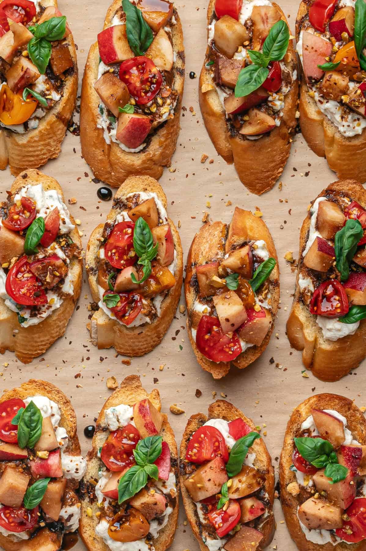 Slices of toasted bread topped with creamy ricotta, diced tomatoes, chopped apples, fresh basil leaves, and a drizzle of balsamic vinegar—this ricotta bruschetta is artfully arranged on a parchment paper background.