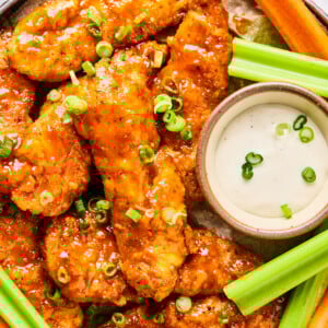 A plate of crispy Air Fryer Buffalo Chicken Tenders garnished with chopped green onions, served with celery, carrot sticks, and a bowl of ranch dipping sauce.