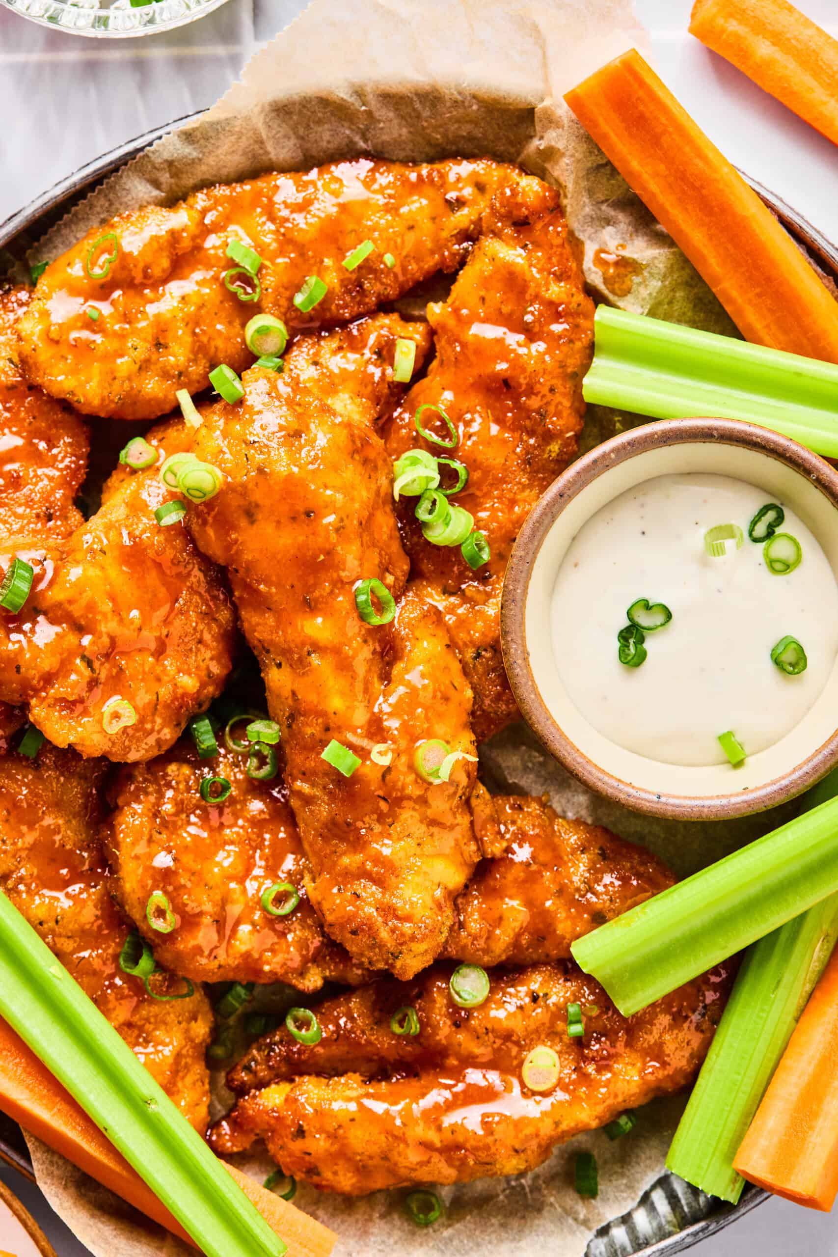 A plate of crispy Air Fryer Buffalo Chicken Tenders garnished with chopped green onions, served with celery, carrot sticks, and a bowl of ranch dipping sauce.
