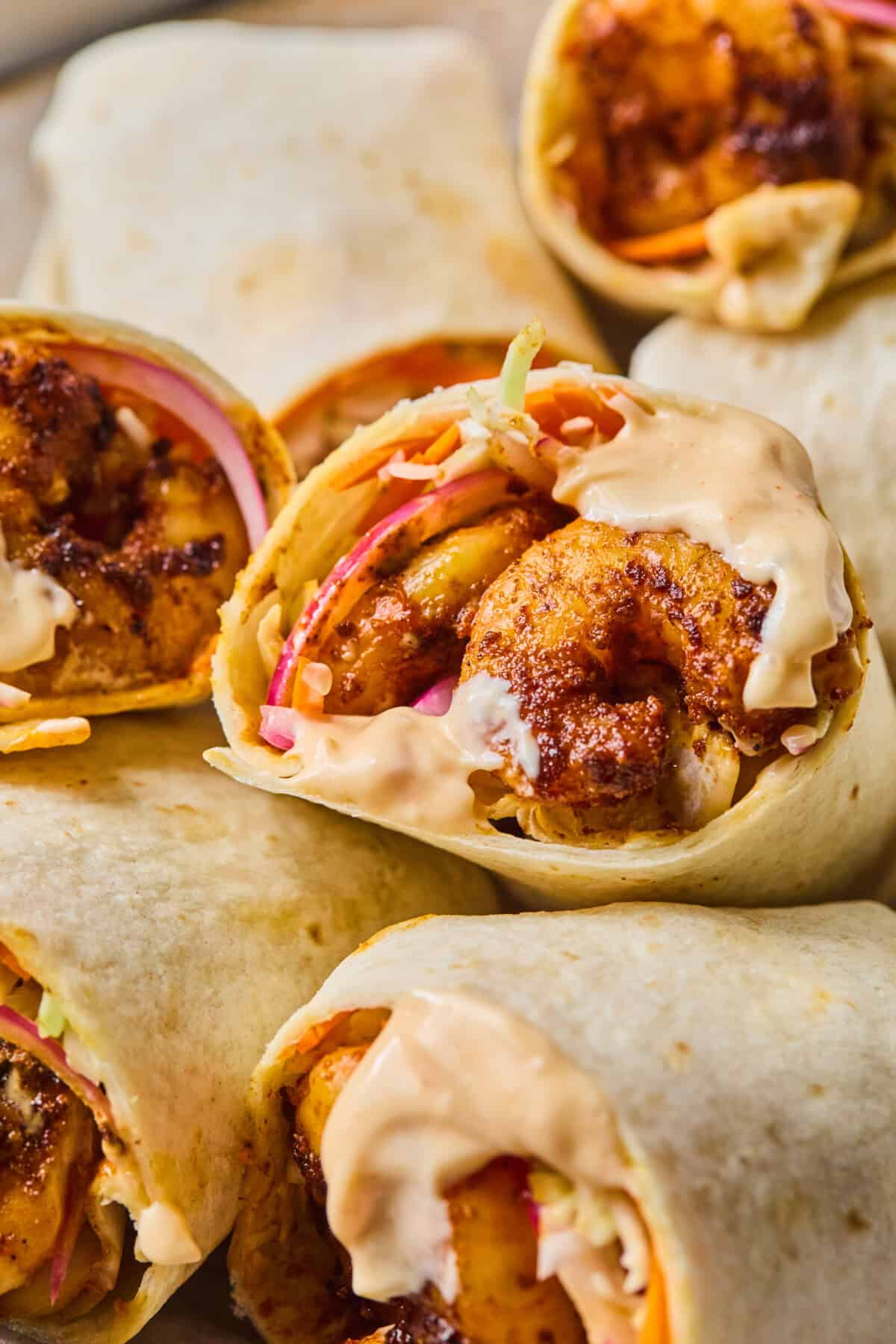 Close-up of Shrimp Wraps filled with seasoned shrimp, shredded vegetables, and creamy sauce, cut in half to reveal the colorful filling inside. The wraps are stacked together, highlighting their fresh ingredients.