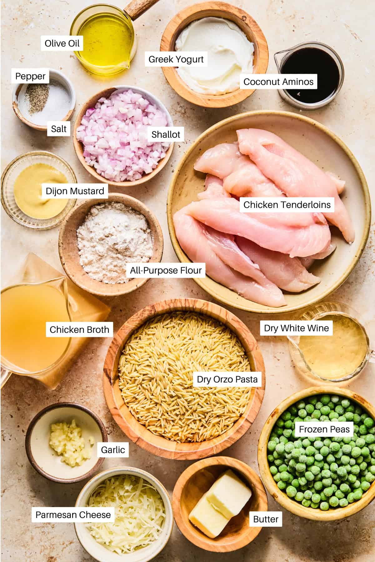 A top-down view of labeled ingredients for a delicious chicken and peas recipe, featuring chicken tenderloins, dry orzo pasta, Greek yogurt, coconut aminos, chicken broth, frozen peas, garlic, olive oil, butter, and more.
