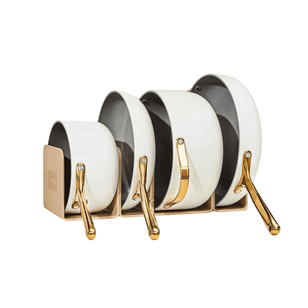 Four white and gold-handled pots and pans of different sizes are neatly stacked in a wooden organizer against a white background.