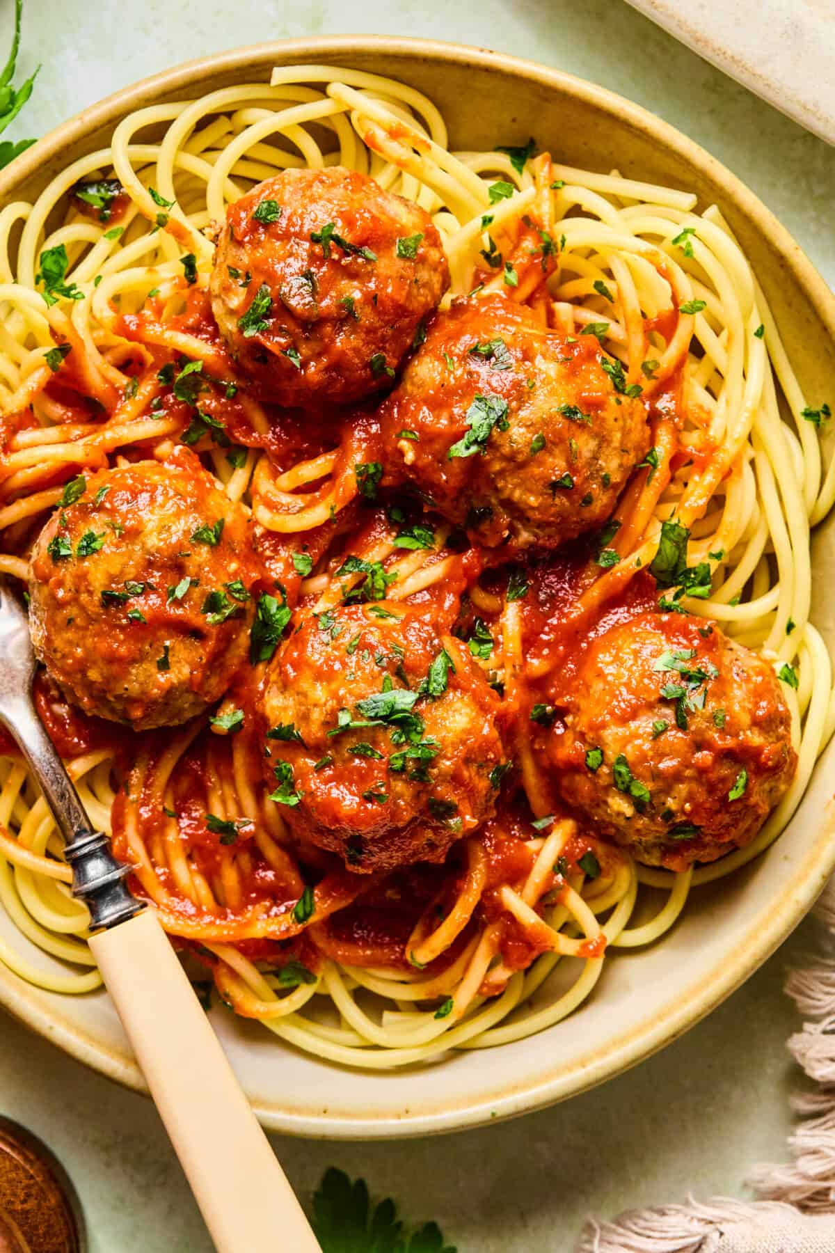 A plate of spaghetti topped with five baked turkey meatballs in tomato sauce, garnished with chopped parsley. A fork and knife rest on the edge of the plate.