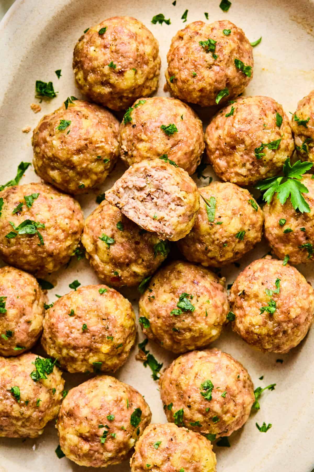 A platter of golden-brown baked turkey meatballs garnished with chopped parsley, with one meatball cut in half to reveal the juicy, tender inside.