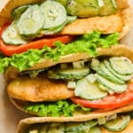 Three pita bread sandwiches filled with lettuce, tomato slices, grilled chicken, and a creamy cucumber salad with dill and cheese are arranged closely together on a light surface—a fresh take on any pita wrap recipe.