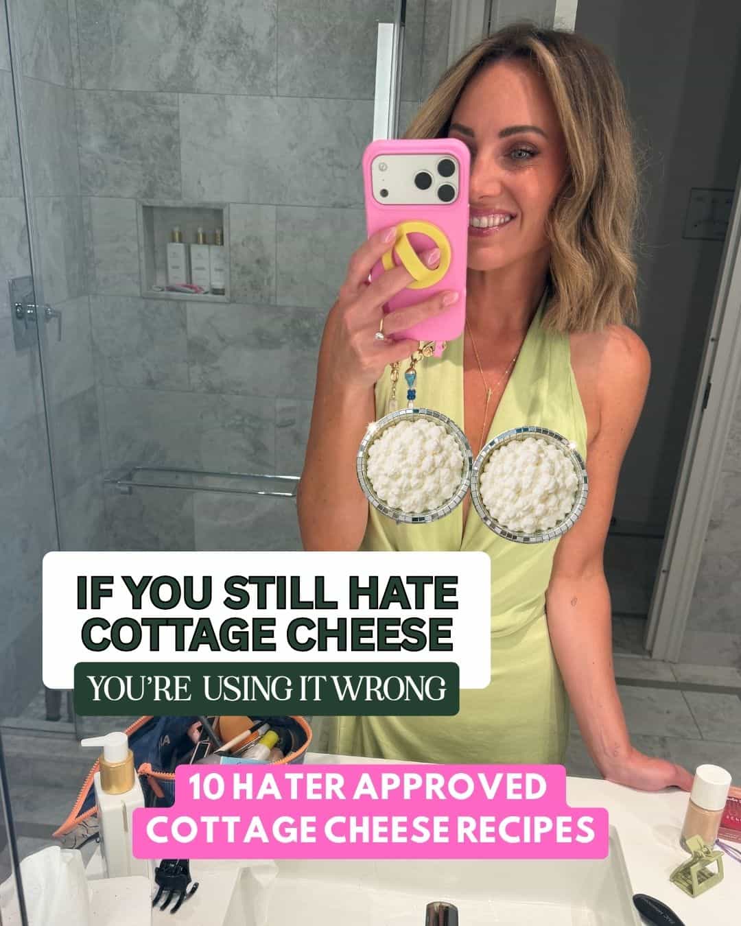 A smiling woman in a bathroom holds a phone and wears earrings resembling bowls of cottage cheese. Text reads: If you still hate cottage cheese, you’re using it wrong. 10 hater approved high protein cottage cheese recipes.
