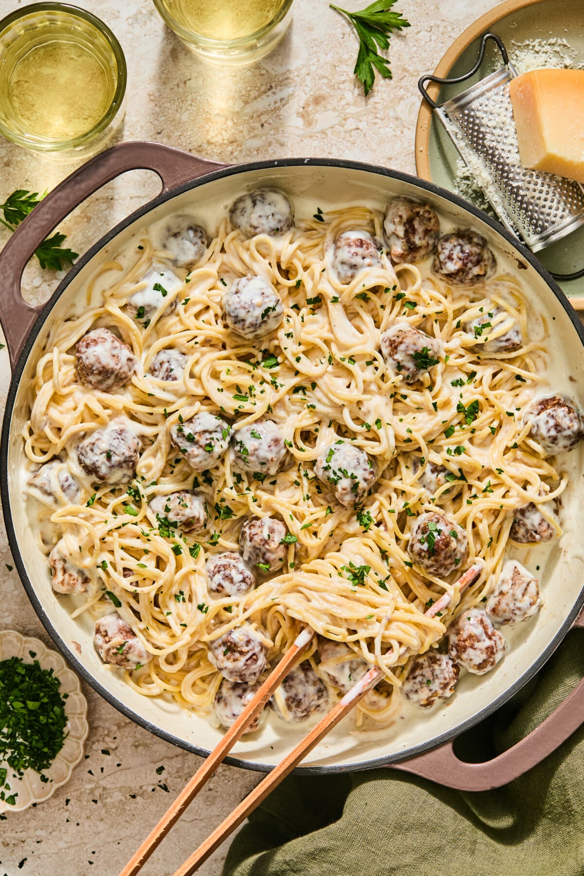 Alfredo spaghetti and meatballs in a creamy sauce, garnished with parsley in a large skillet, with a grater and parmesan cheese nearby.