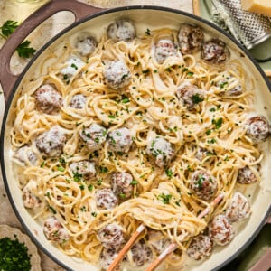 Alfredo spaghetti and meatballs in a creamy sauce, garnished with parsley in a large skillet, with a grater and parmesan cheese nearby.
