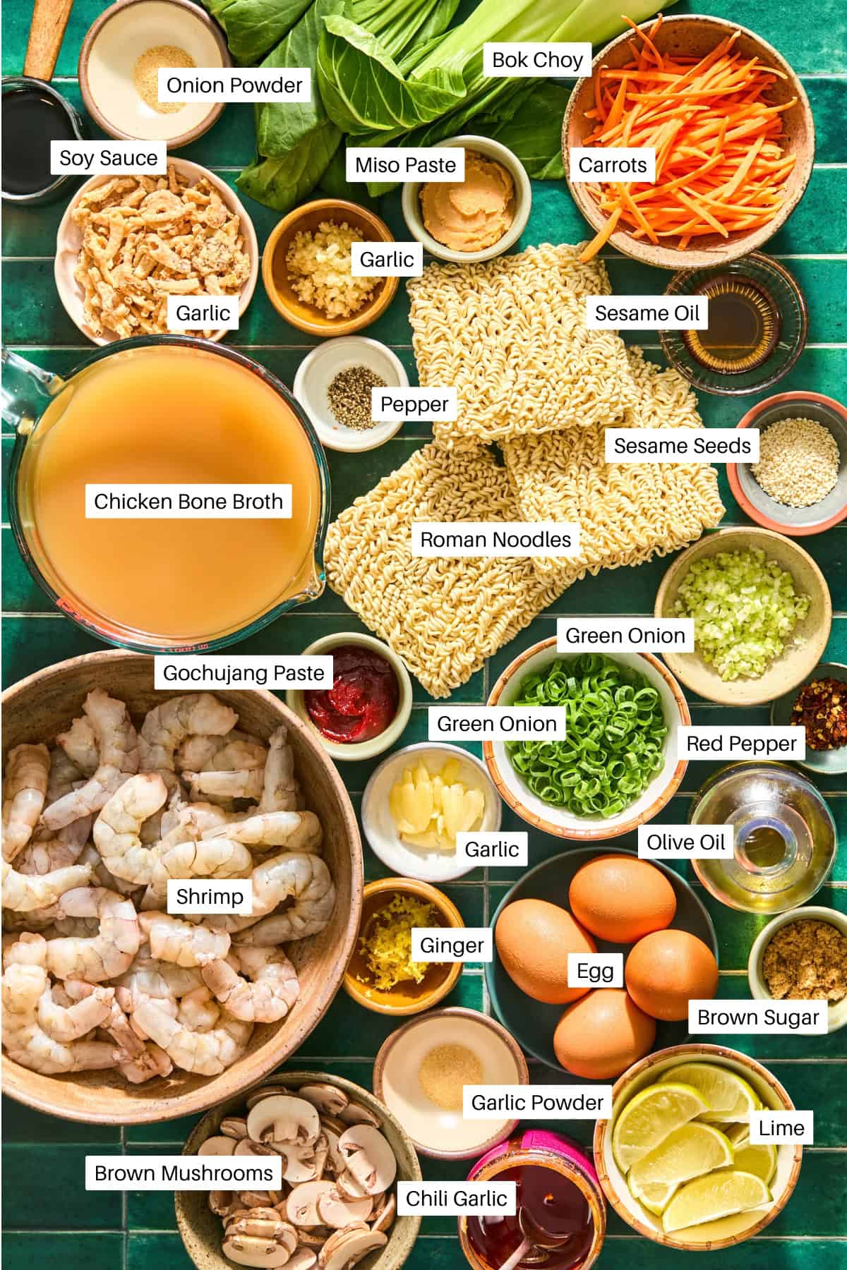 Assorted ramen ingredients for Spicy Shrimp Ramen including shrimp, eggs, ramen noodles, bok choy, broth, mushrooms, spices, sauces, and vegetables arranged on a table with labeled names.