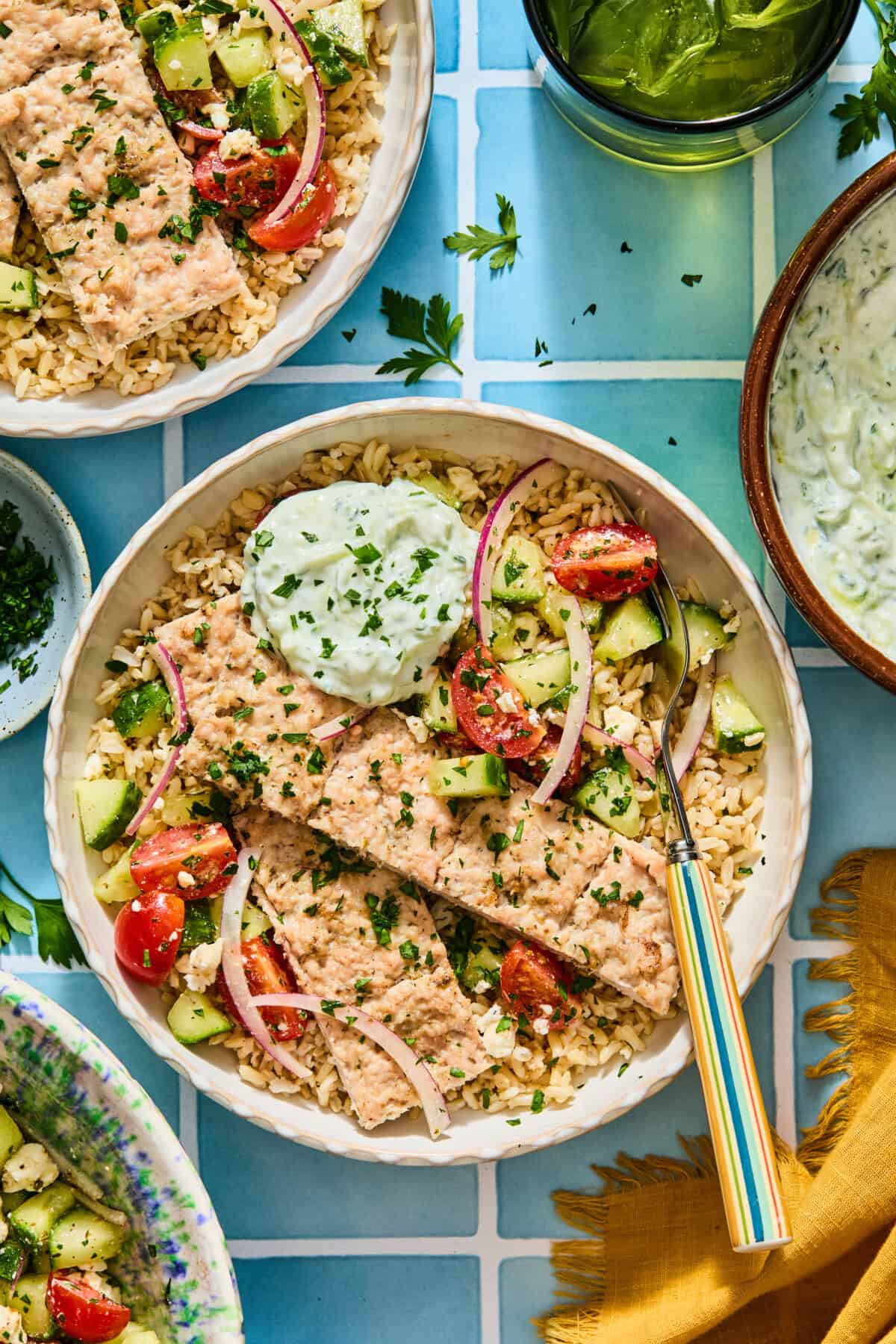 A gyro bowl of rice topped with salmon fillets, cucumber tomato salad, and a dollop of tzatziki sauce.