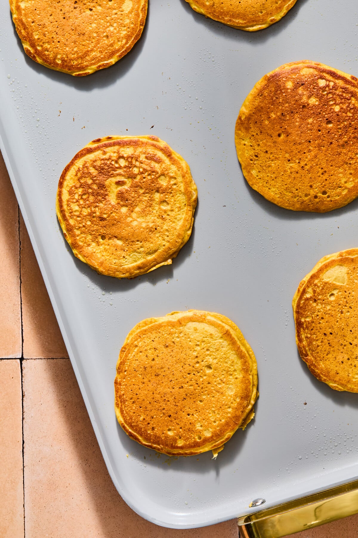 Five golden-brown pumpkin pancakes cooking on a flat griddle.