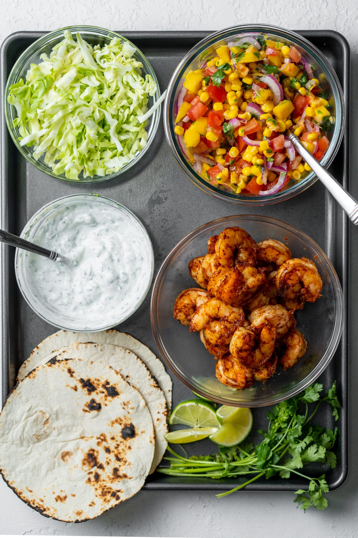 Tray with mango corn salsa, shrimp, lettuce, and other taco ingredients.