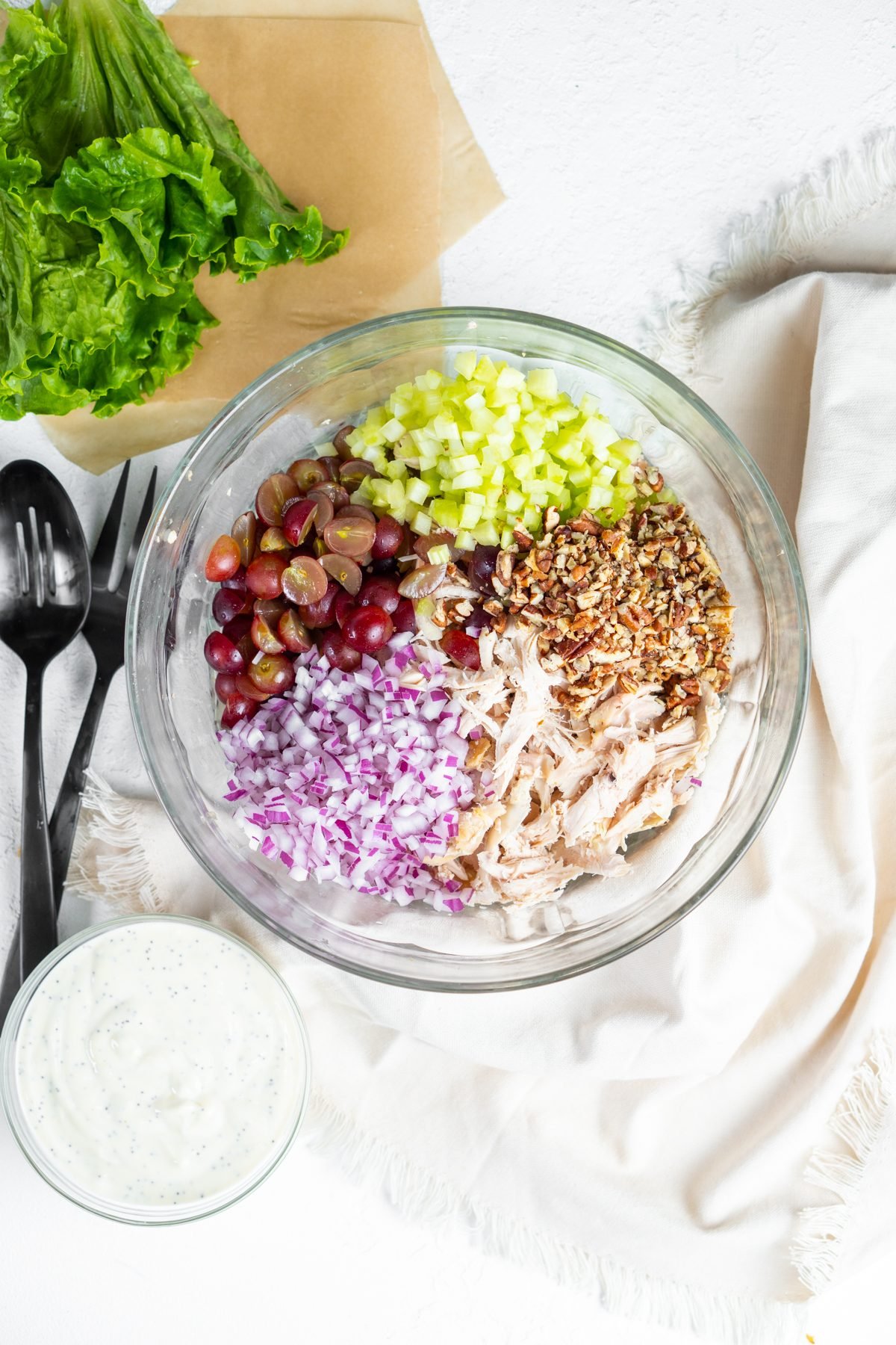 Bowl of unmixed California chicken salad ingredients including red onion and grapes.