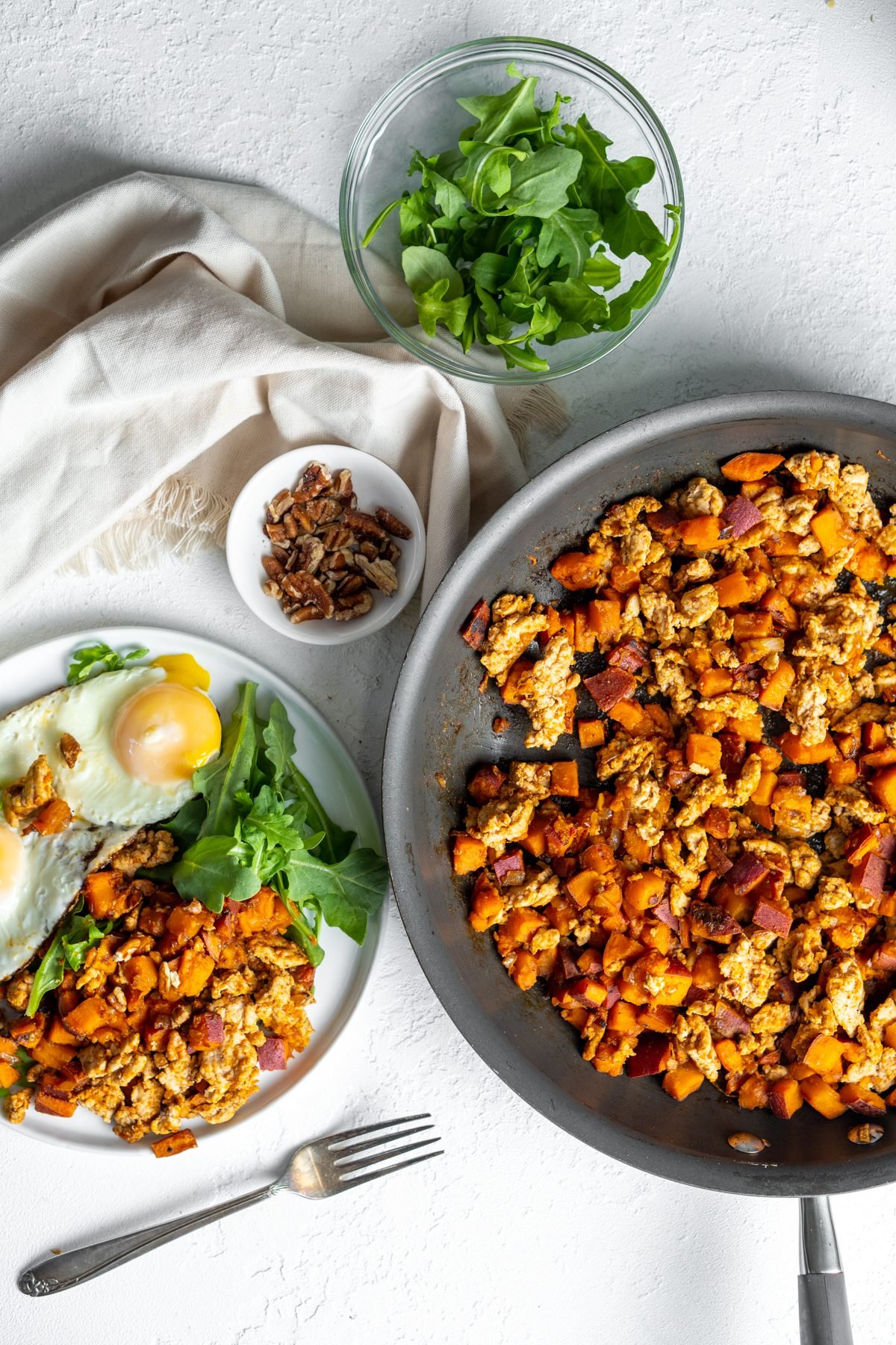 Greens, turkey sweet potato hash, and eggs set on a table.