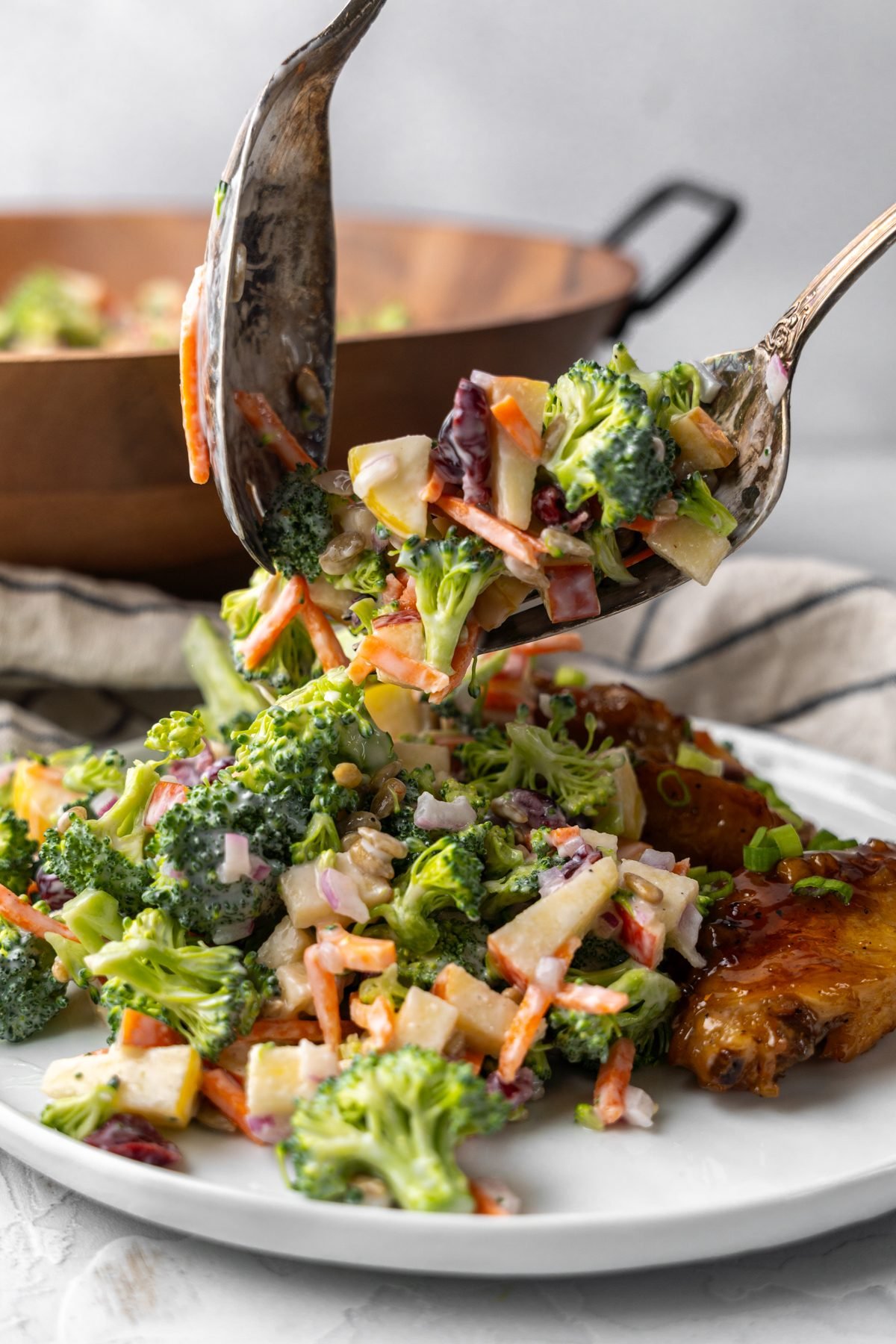 Spoons scooping broccoli crunch salad onto a plate.