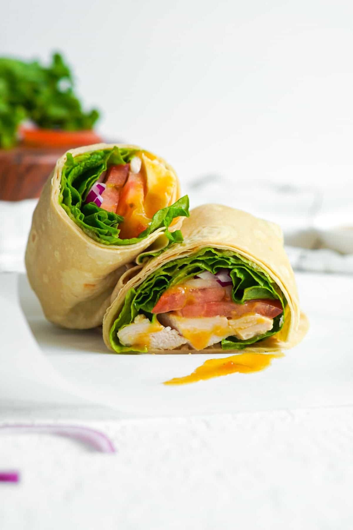 Halved honey mustard chicken wrap leaning against the other half on parchment paper.