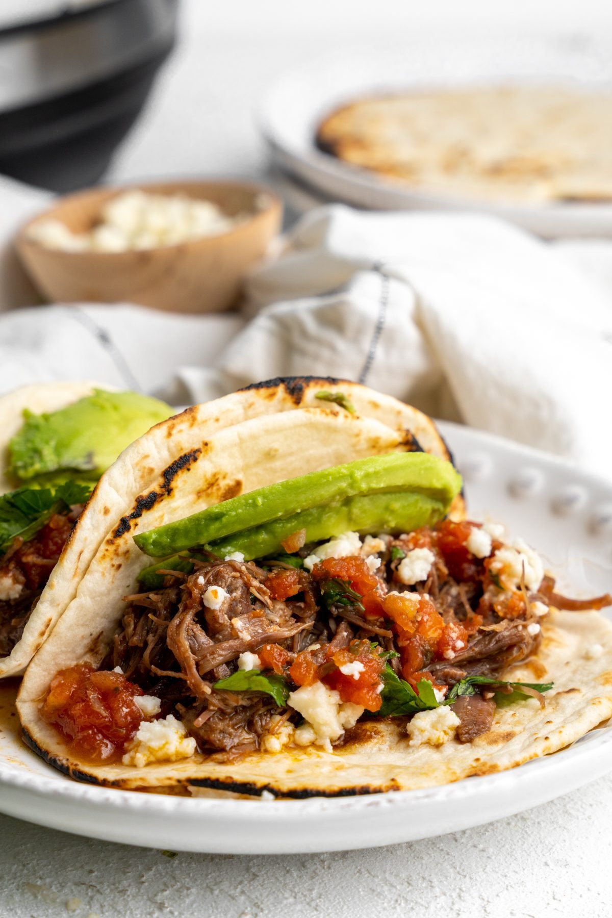 Shredded beef tacos on a white plate.