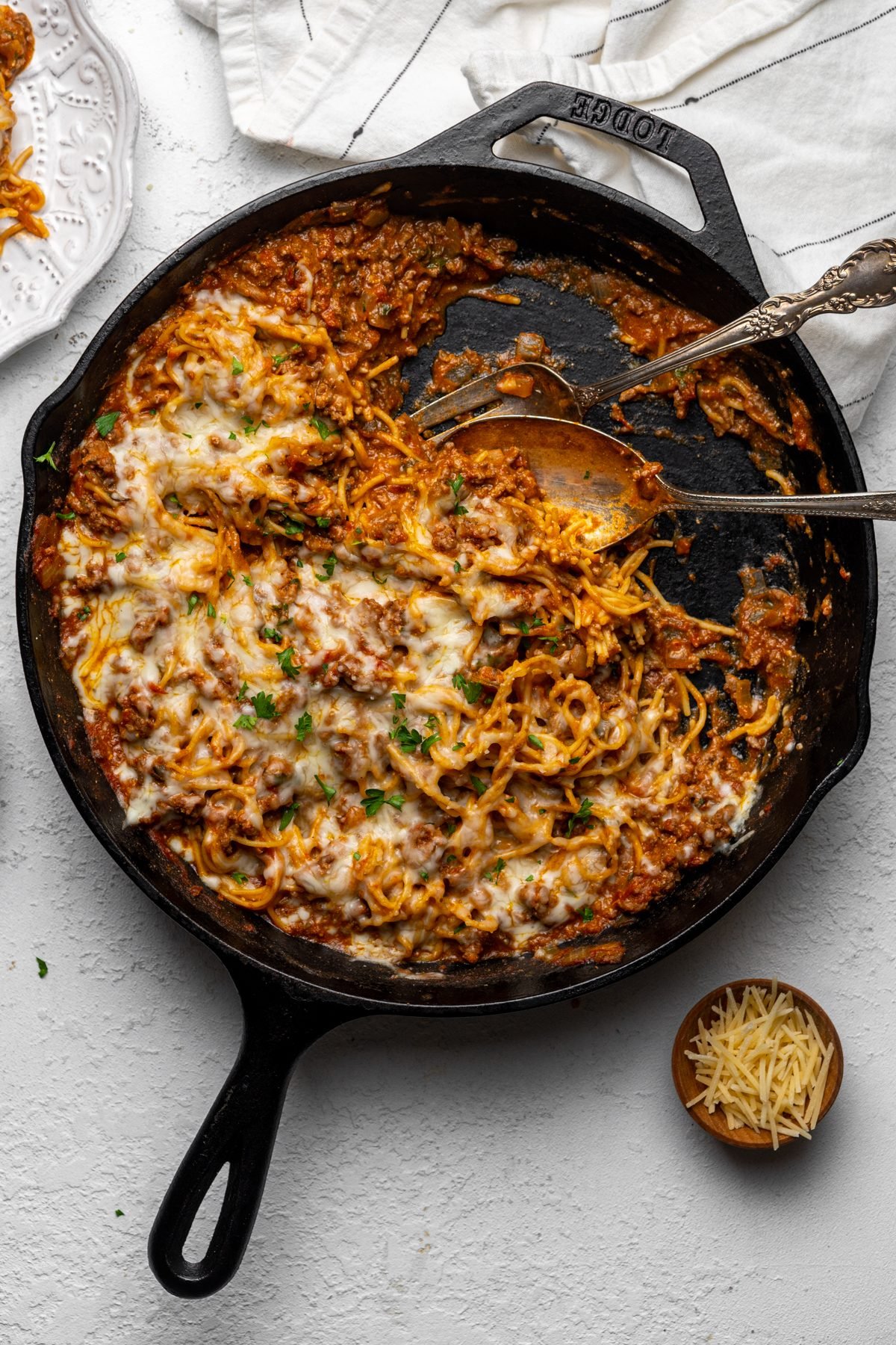Serving utensils in a partially-served skillet of fried spaghetti.