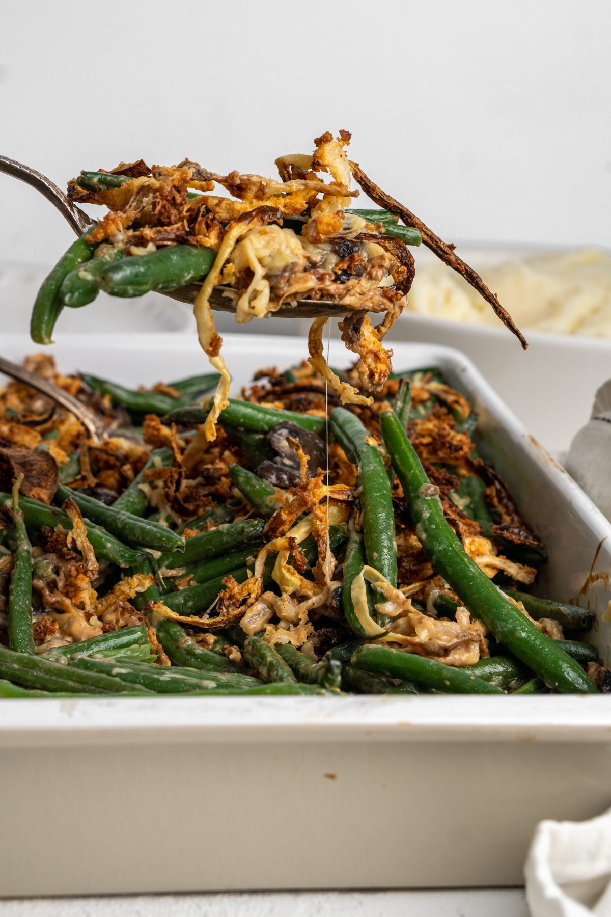 Spoon scooping a serving of cheesy green beans with crispy onions on top. 
