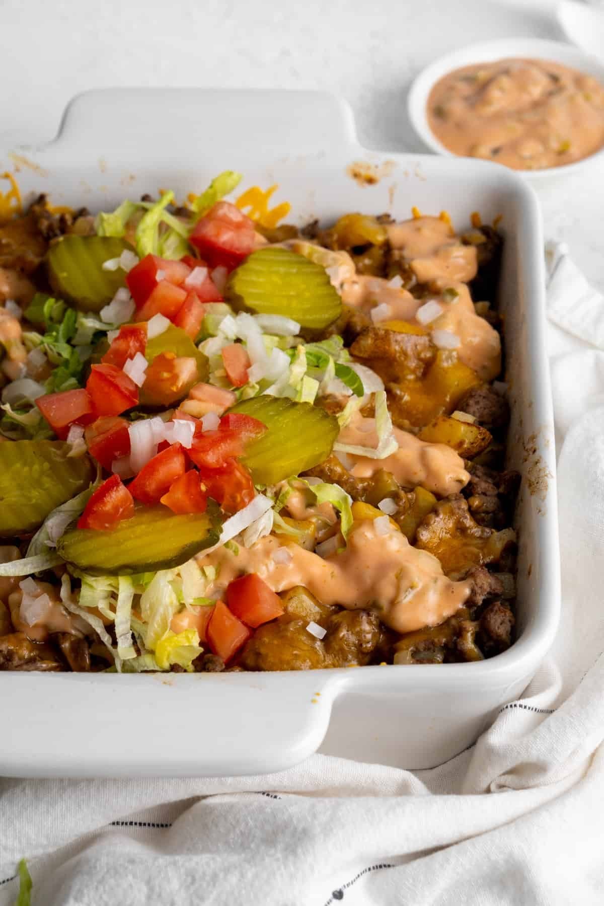Big mac casserole topped with pickles, lettuce, and tomatoes.