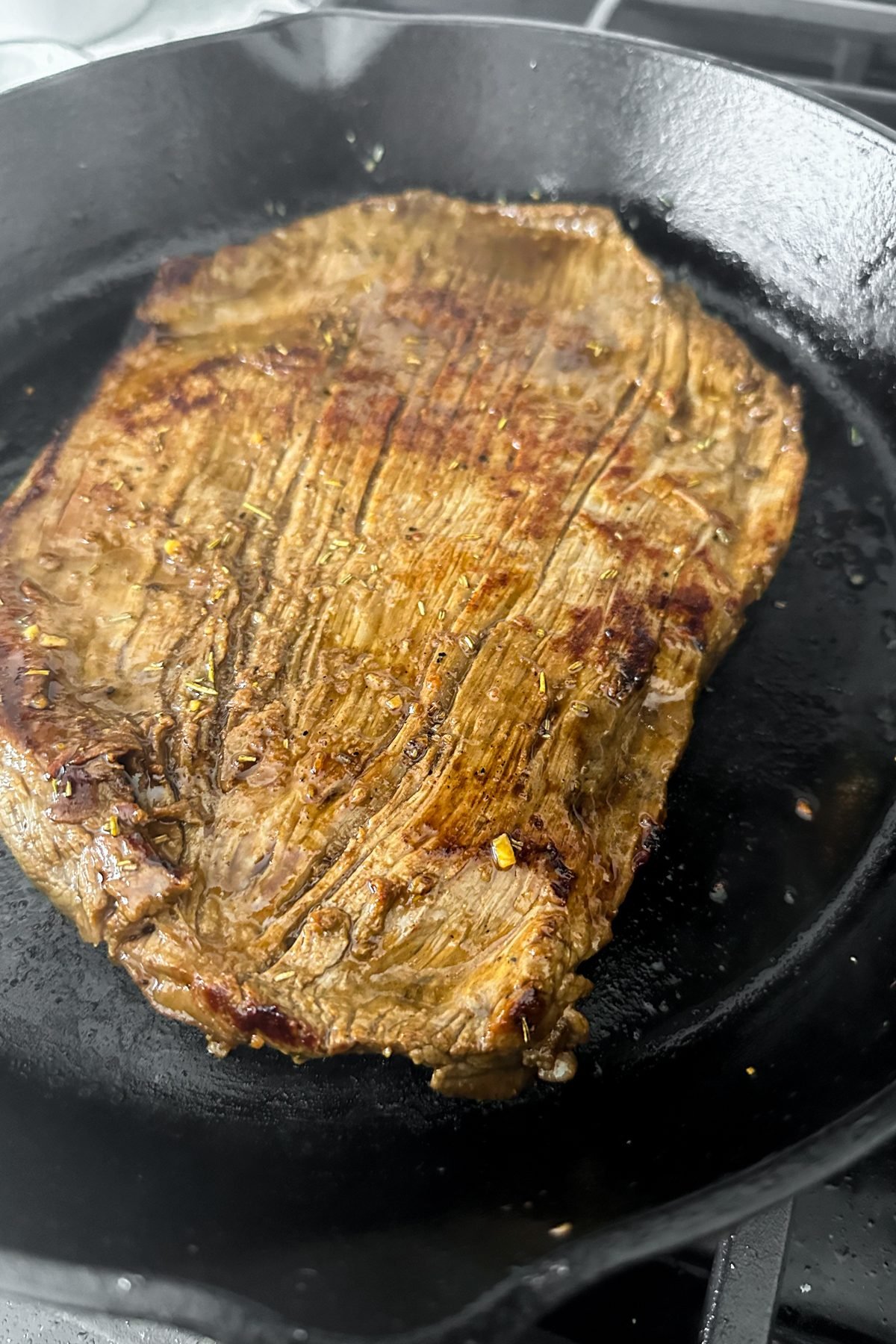 Flank steak being seared in a pan.