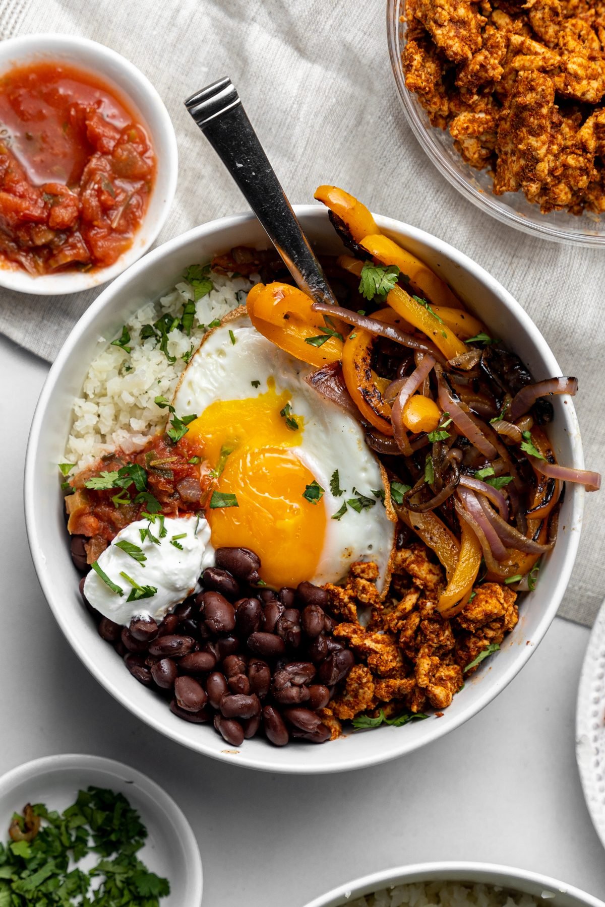Fork in a breakfast burrito bowl with beans, egg, vegetables, and more.